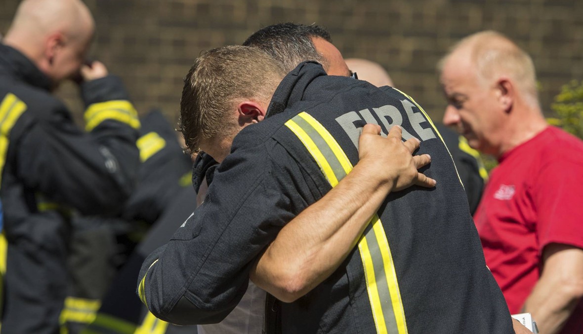 عناق بين رجل اطفاء ومواطن في لندن بعد وقوف دقيقة صمت حداداً على ضحايا حادثة حريق البرج غرب لندن الاسبوع الماضي ( الصورة نقلاً عن afp)