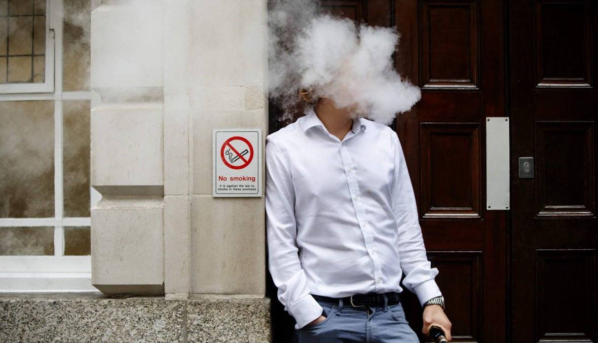 موظف في لندن يدخن سيجارته الالكترونية وقت الغداء قرب لافتة كتب عليها: "ممنوع التدخين".(الصورة نقلاً عن أ. ف. ب)