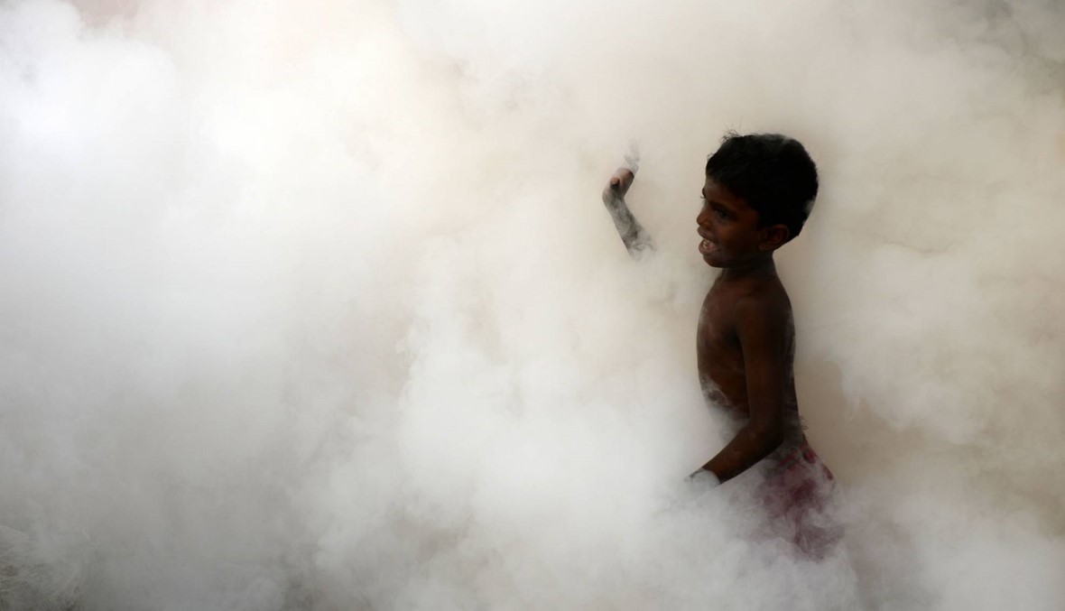 طفل هندي يتبع عامل البدلية اثناء رشه للمبيدات في احد الاحياء الصينية (أ ف ب)