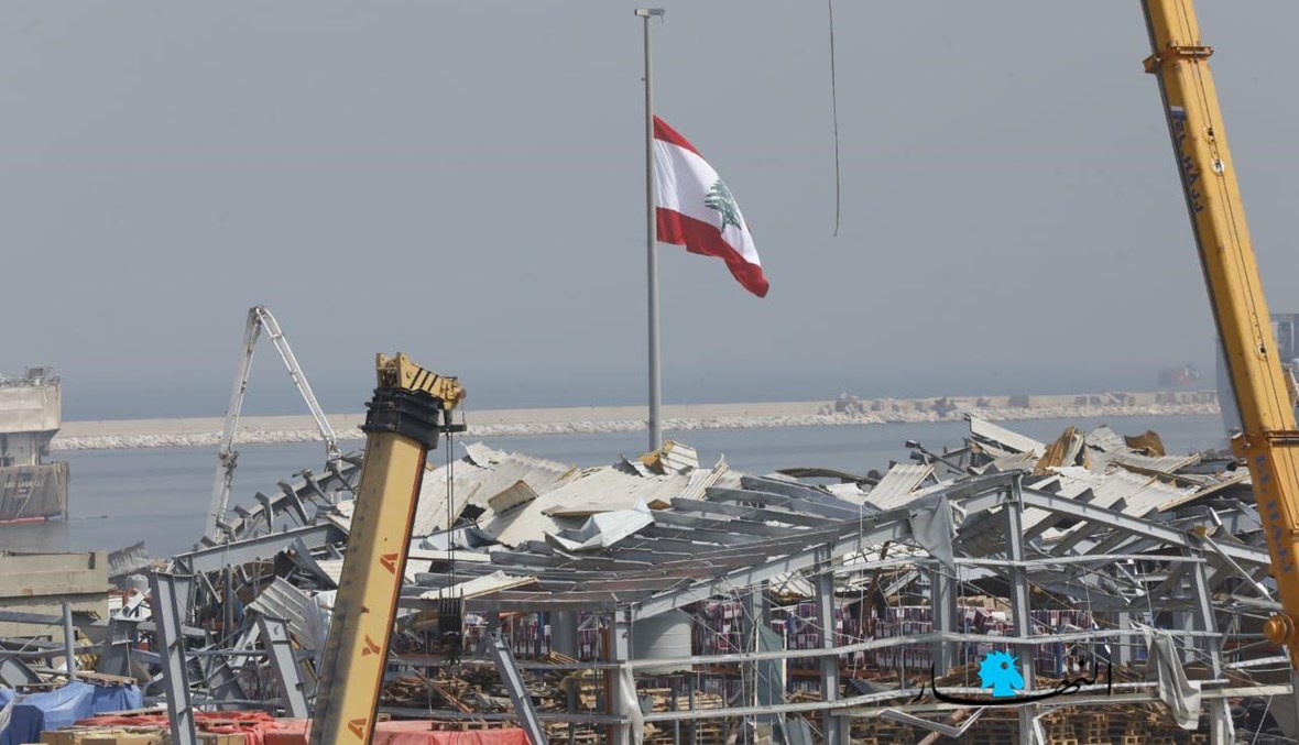 العلم اللبناني فوق أنقاض المرفأ بعد شهر على الفاجعة.