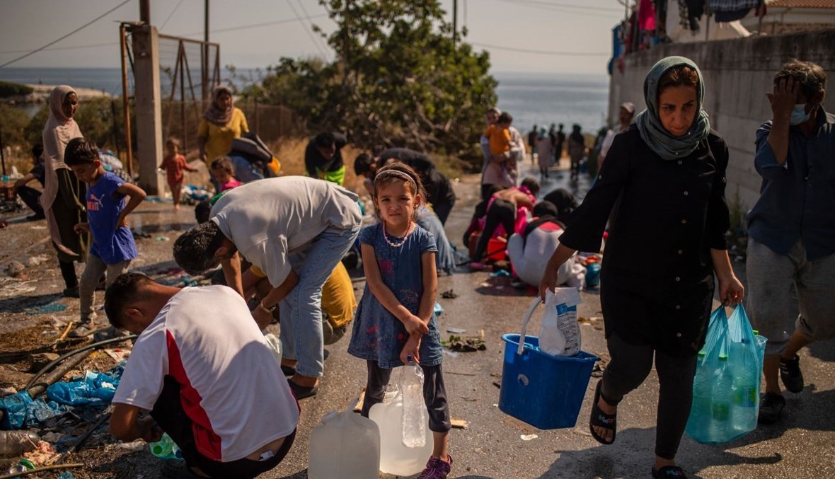 مهاجرون يملأون زجاجات بالمياه بالقرب من مخيم موقت للمهاجرين في جزيرة ليسبوس اليونانية (16 أيلول 2020، أ ف ب). 