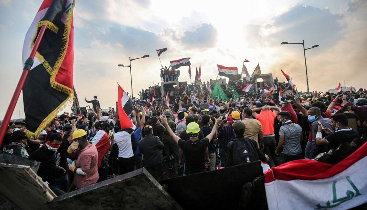 صورة مؤرخة في 29 تشرين الأول 2019 لمتظاهرين عراقيين يرفعون الإعلام الوطنية على جسر الجمهورية في بغداد.   (أ ف ب)