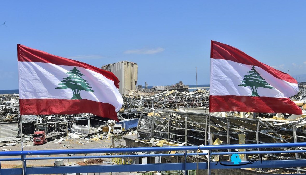 العلم اللبناني مقابل المرفأ المدمّر ("النهار").