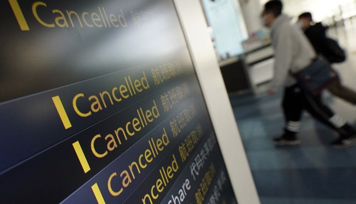 Travelers walk past canceled flights on a schedule board, some due to the coronavirus, at the Haneda International Airport in Tokyo, Wednesday, March 18, 2020. (AP Photo)