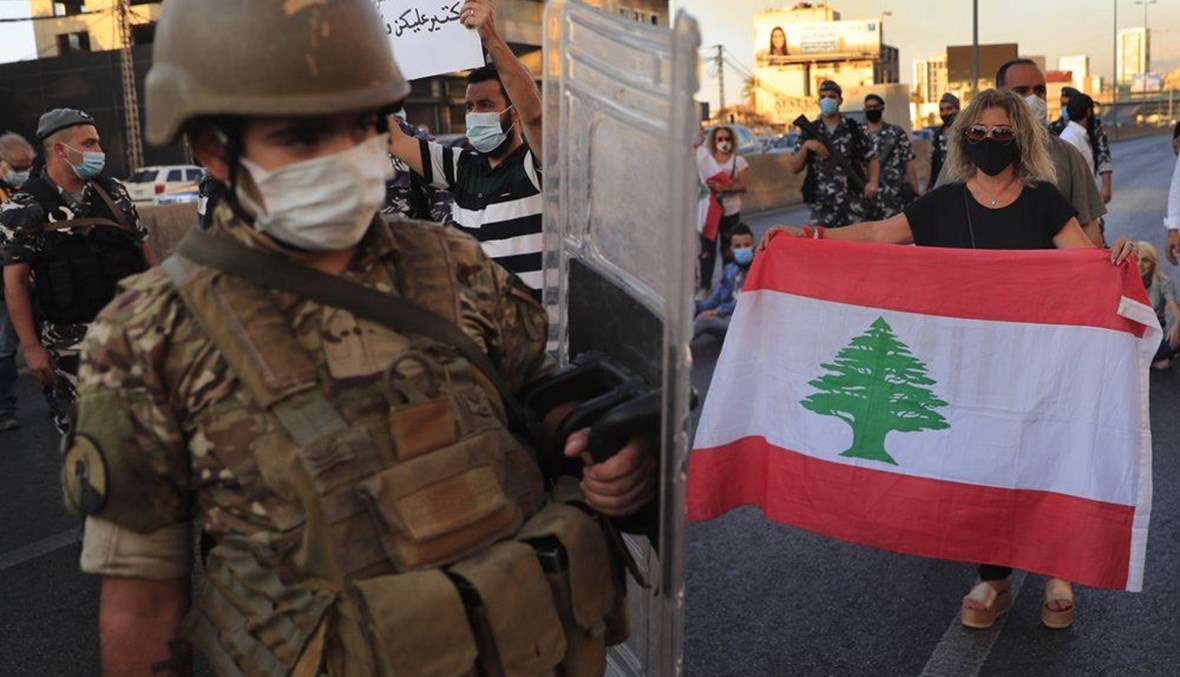 A Lebanese army soldier passes in front of an anti-government protester holding a national flag and blocking a main highway in Zalka on October 5,2020. (AP Photo)
