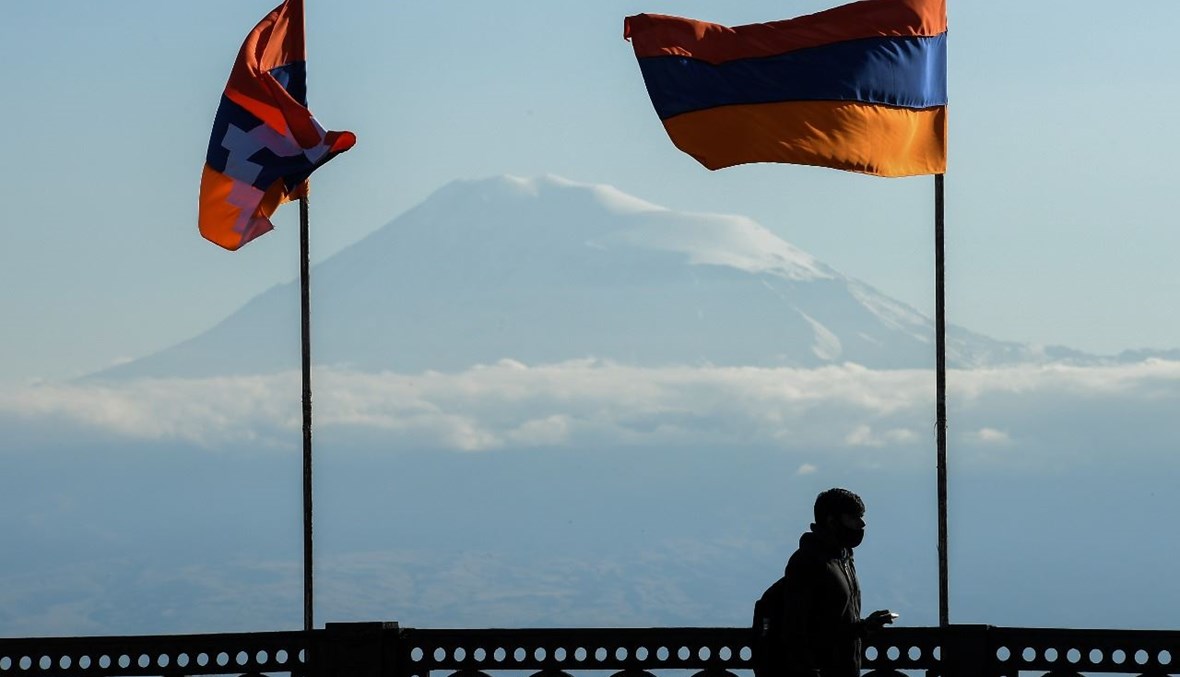 رجل يمشي على جسر في يريفان زيّن بأعلام أرمينيا ومنطقة ناغورنو قره باغ المنفصلة. وبدا جبل أرارات في الخلفية (7 ت1  2020، أ ف ب). 