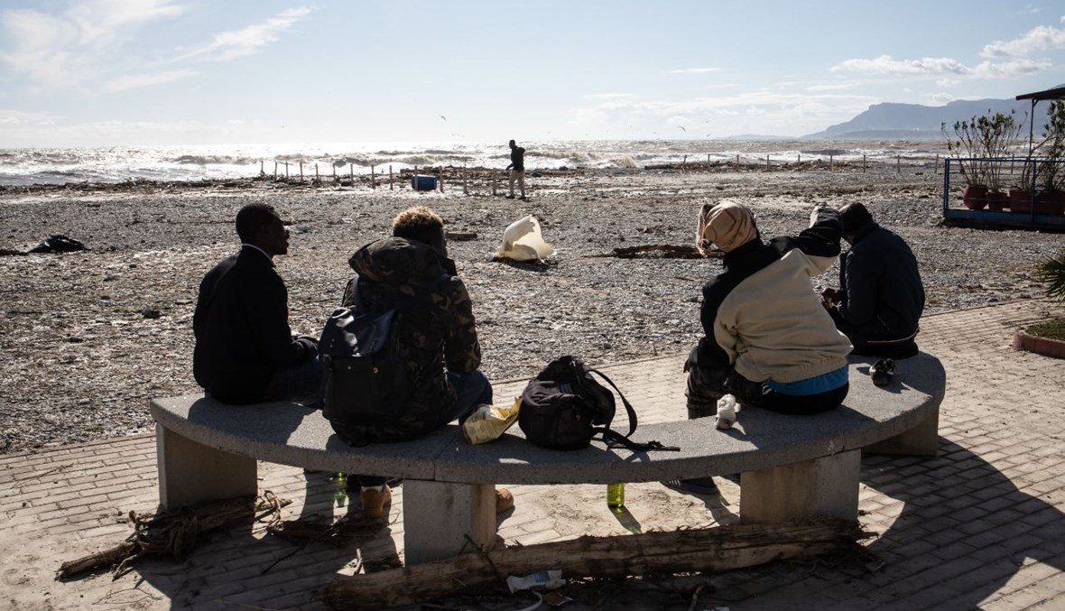 مجموعة من المهاجرين تجلس على الشاطئ في فينتيميليا بإيطاليا بعدما غمر نهر رويا المدينة بأكملها بالماء والطين (3 ت1 2020، أ ف ب). 