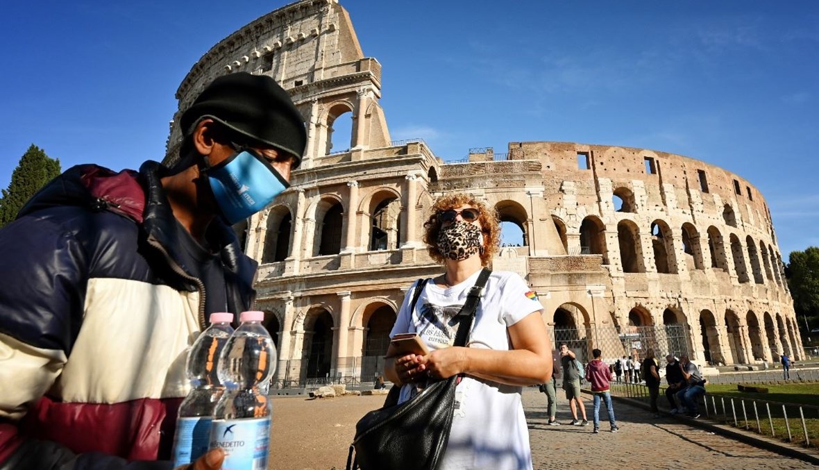 بائع متجوّل وامرأة يمران بالقرب من الكولوسيوم في روما (9 ت1 2020، أ ف ب). 
