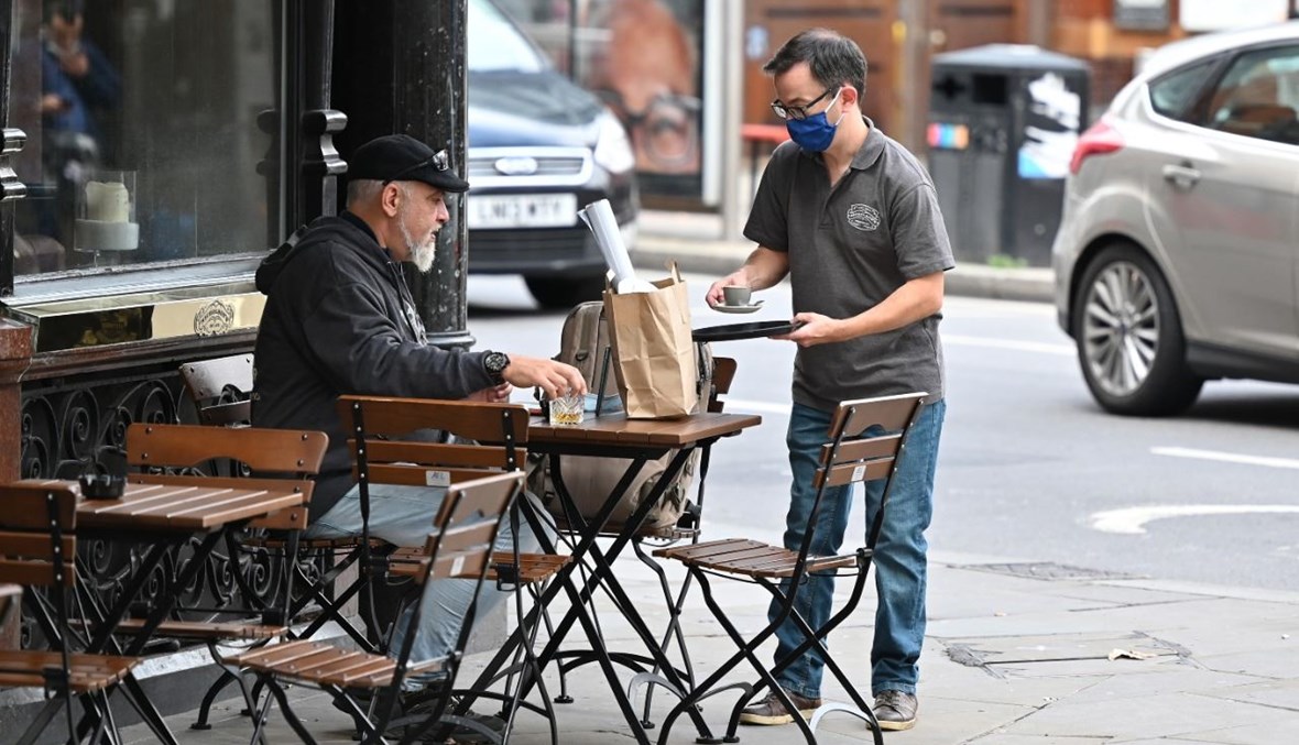 نادل يقدم القهوة إلى رجل جلس خارج حانة في غرب لندن (11 ت1 2020، أ ف ب). 
