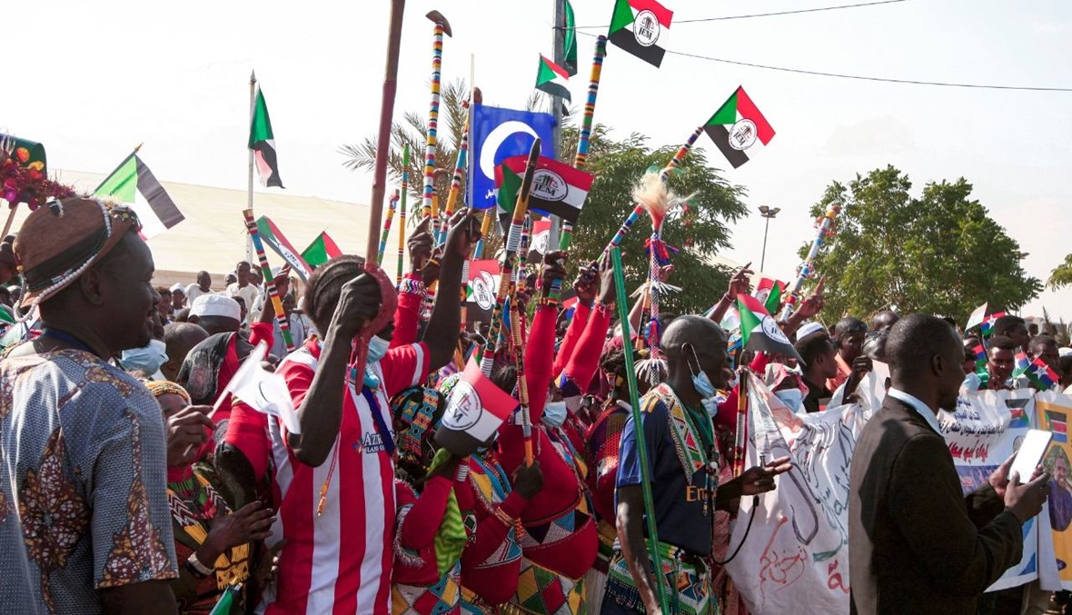 أشخاص يلوحون بأعلام السودان في الخرطوم خلال استقبال فريق المفاوضات الحكومي العائد من جوبا (8 ت1 2020، أ ف ب). 