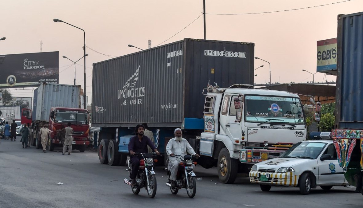 سائقو دراجات نارية يمرون بالقرب من شاحنات متوقفة قبل حاجز بالقرب من الطريق السريع في لاهور (15 ت1 2020، أ ف ب). 
