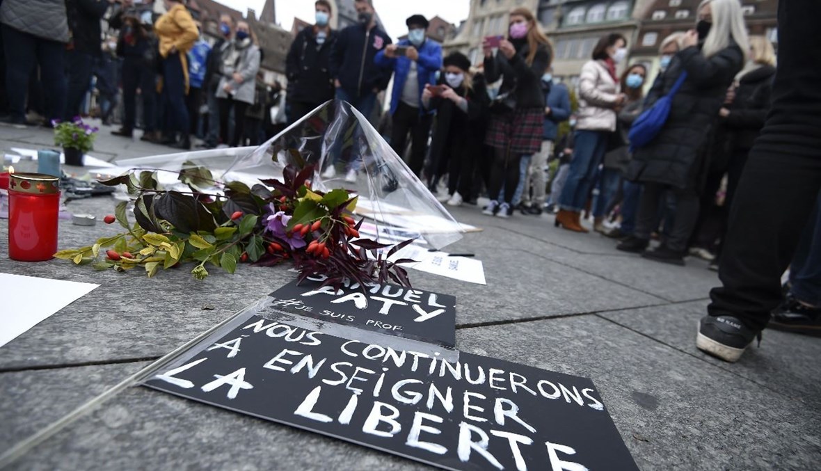 أشخاص وقفوا بالقرب من الزهور ولافتات كتب عليها "سنواصل تعليم الحرية"، خلال تجمع في ستراسبورغ شرق فرنسا تكريما للمدرس الفرنسي صمويل باتي (18 ت1 2020، أ ف ب). 