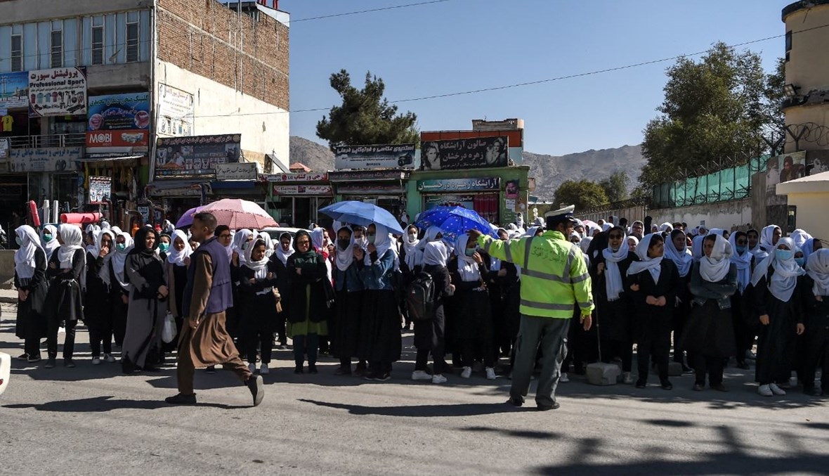طالبات ينتظرن عند جانب الطريق بينما يعبر مسؤولون حكوميون (ليسوا في الصورة) الطريق بالقرب من البرلمان في كابول (21 ت1 2020، ا ف ب).