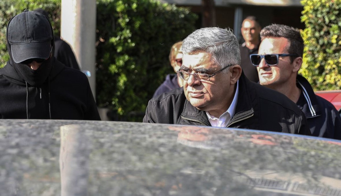 زعيم حزب النازيين الجدد اليوناني نيكوس ميخالولياكوس يرافقه عناصر من الشرطة الى السيارة ليسلم نفسه في أثينا (22 ت1 2020، أ ف ب). 