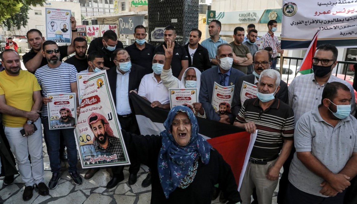 متظاهرون فلسطينيون يرفعون صور الأخرس خلال تجمع تضامني معه في وسط مدينة الخليل بالضفة الغربية (21 ت1 2020، أ ف ب). 