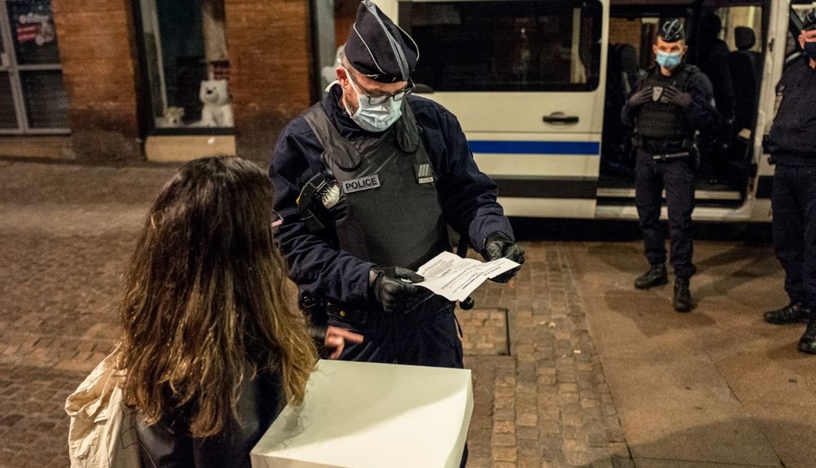شرطي فرنسي يدقق في أوراق امرأة في تولوز جنوب غرب فرنسا، مع بداية حظر التجول بسبب كورونا (24 ت1 2020، أ ف ب). 
