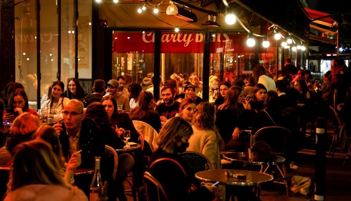 زبائن في مقهى رصيف بوسط باريس قبل سريان حظر التجول الليلي.   (أ ف ب)    