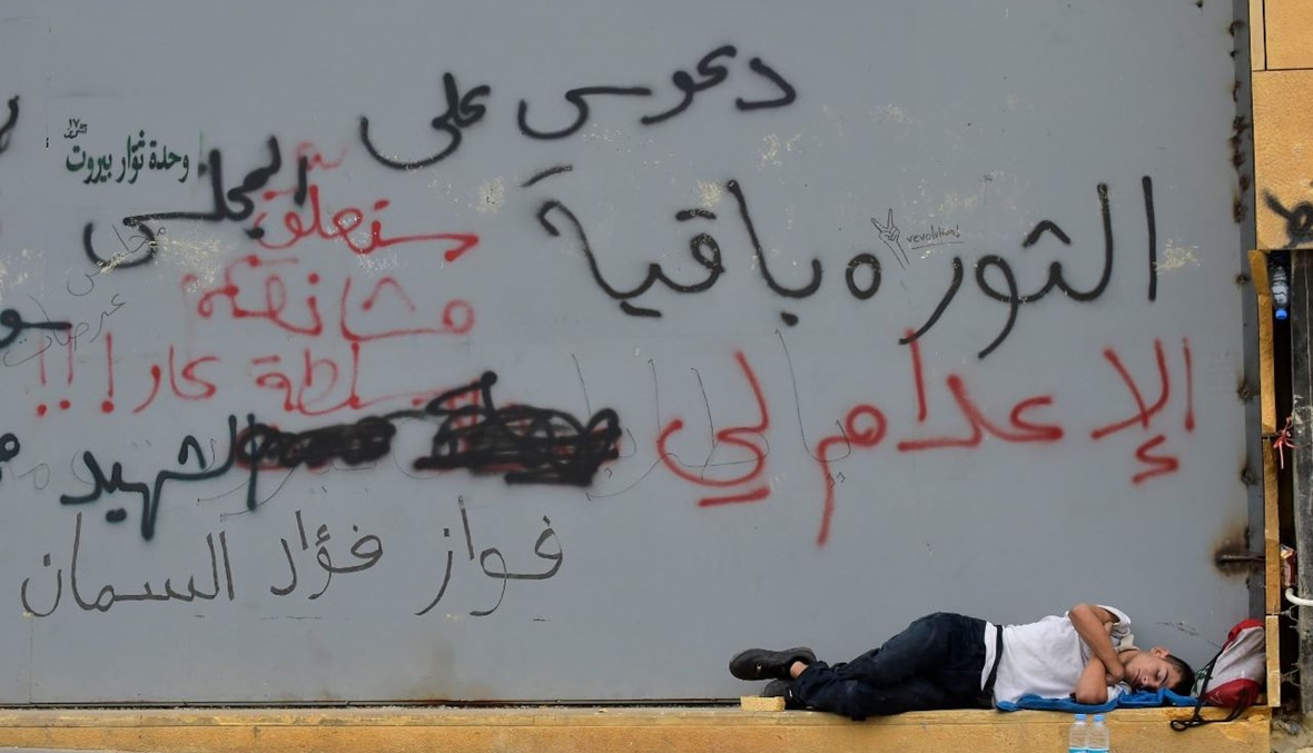 مواطن نائم على قارعة الطريق إلى جانب شعارات من وحي الثورة ("النهار").