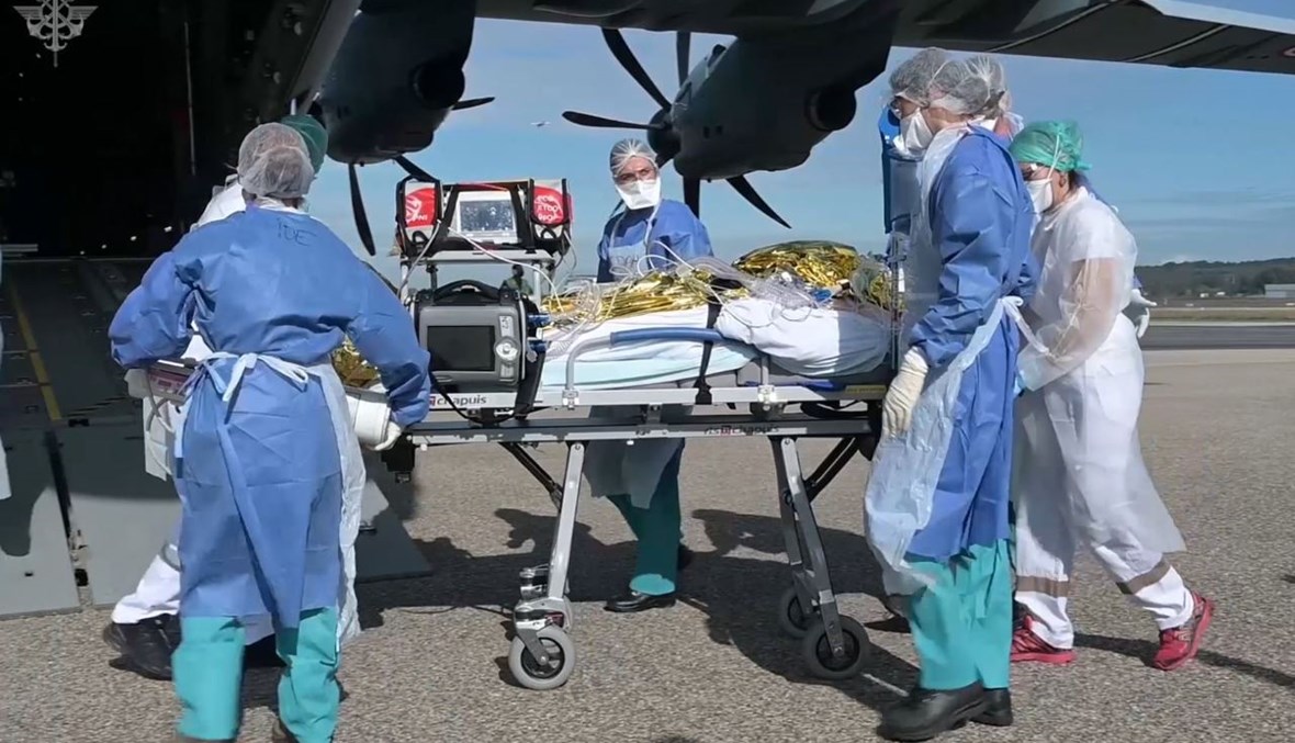 عاملون طبيون ينقلون مريضا مصابا بكورونا بواسطة طائرة مجهزة طبياً في مطار أفينيون جنوب فرنسا (28 ت1 2020، أ ف ب). 