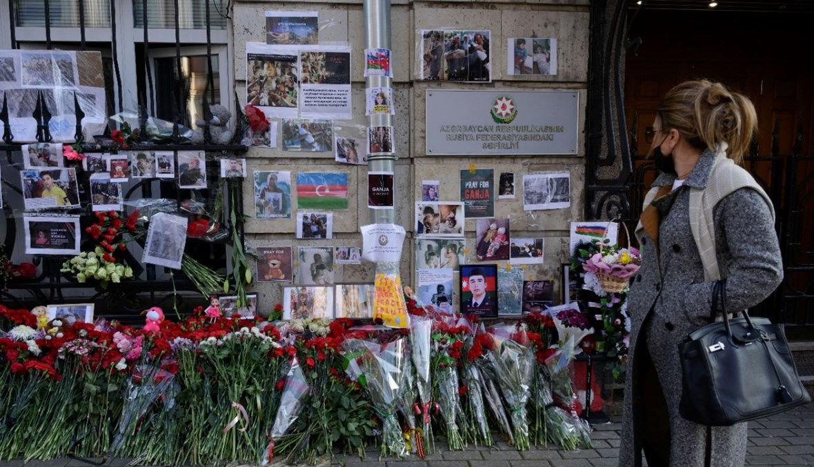 امرأة وقفت بالقرب من باقات زهور وصور لضحايا معارك ناغورنو كراباخ، وضعت عند مدخل السفارة الأذربيجانية في موسكو (28 ت1 2020، أ ف ب). 