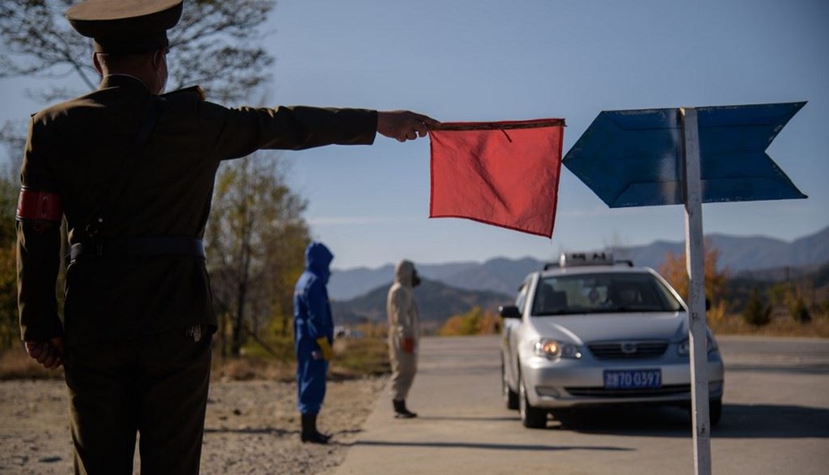 شرطي كوري شمالي يؤشر بعلم أحمر لسيارات كي تتوقف من أجل تعقيمها قبل الدخول إلى مدينة ونسان في إقليم كانغون.(أ ف ب)