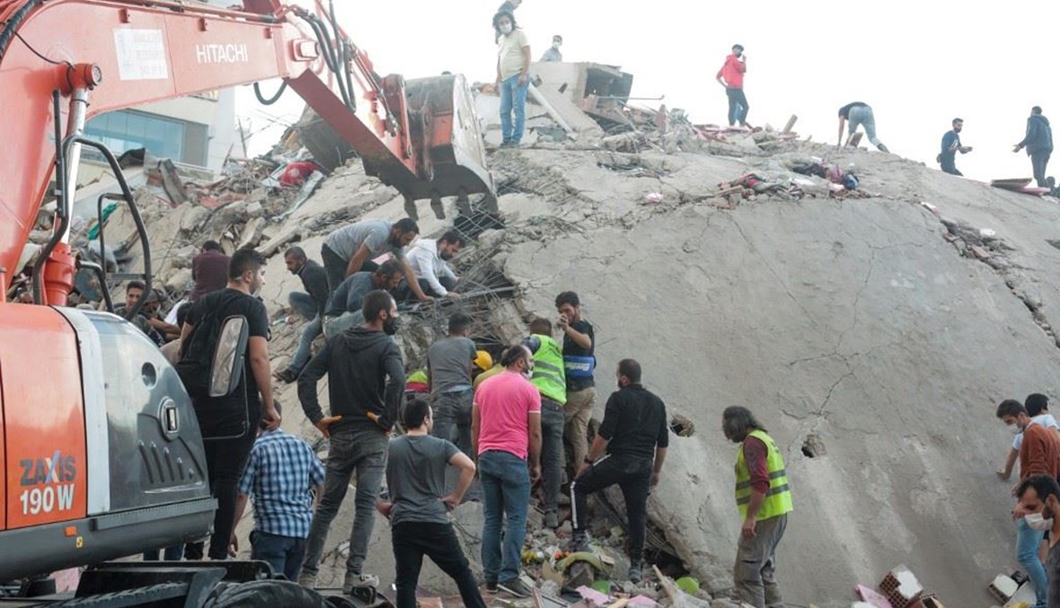 متطوعون يزيلون الأنقاض من مبنى دمر الزلزال في مدينة أزمير التركية أمس.   (أ ف ب)