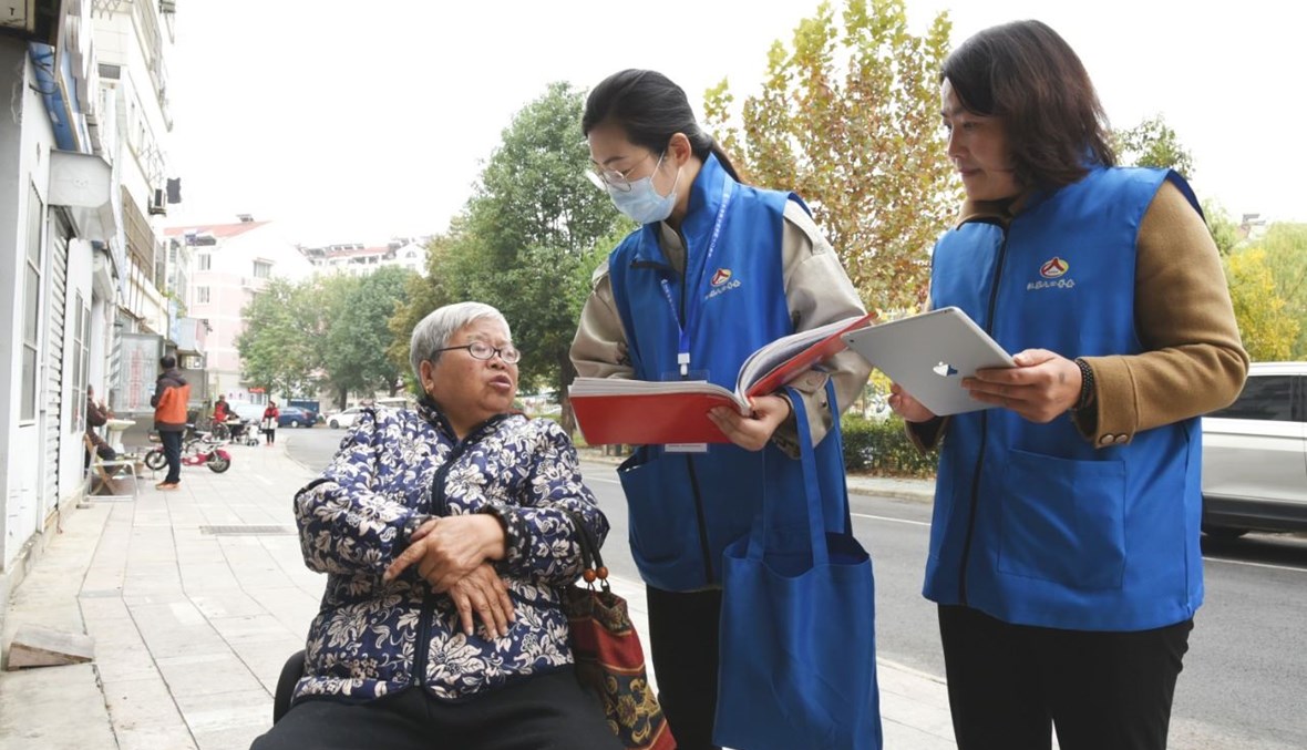 عاملتان تجمعان المعلومات من امرأة في ليانيونغانغ بمقاطعة جيانغسو شرق الصين (1 ت2 2020، أ ف ب).  