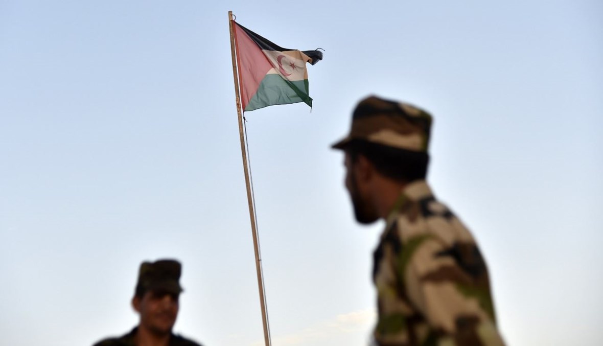 جنديان من جبهة البوليساريو يقفان أمام علم صحراوي في مخيم بوجدور للاجئين بالقرب من مدينة تندوف في غرب الجزائر (17 ت1 2017، أ ف ب). 