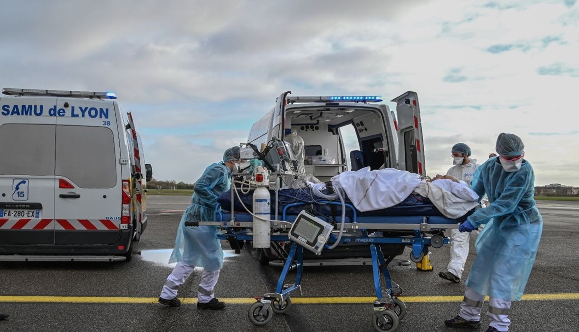 عاملون طبيون ينقلون مريضًا على نقالة في مطار برون بالقرب من ليون جنوب شرق فرنسا، لإيصاله عبر الطائرة إلى مستشفى آخر  (16 ت2 2020، أ ف ب). 