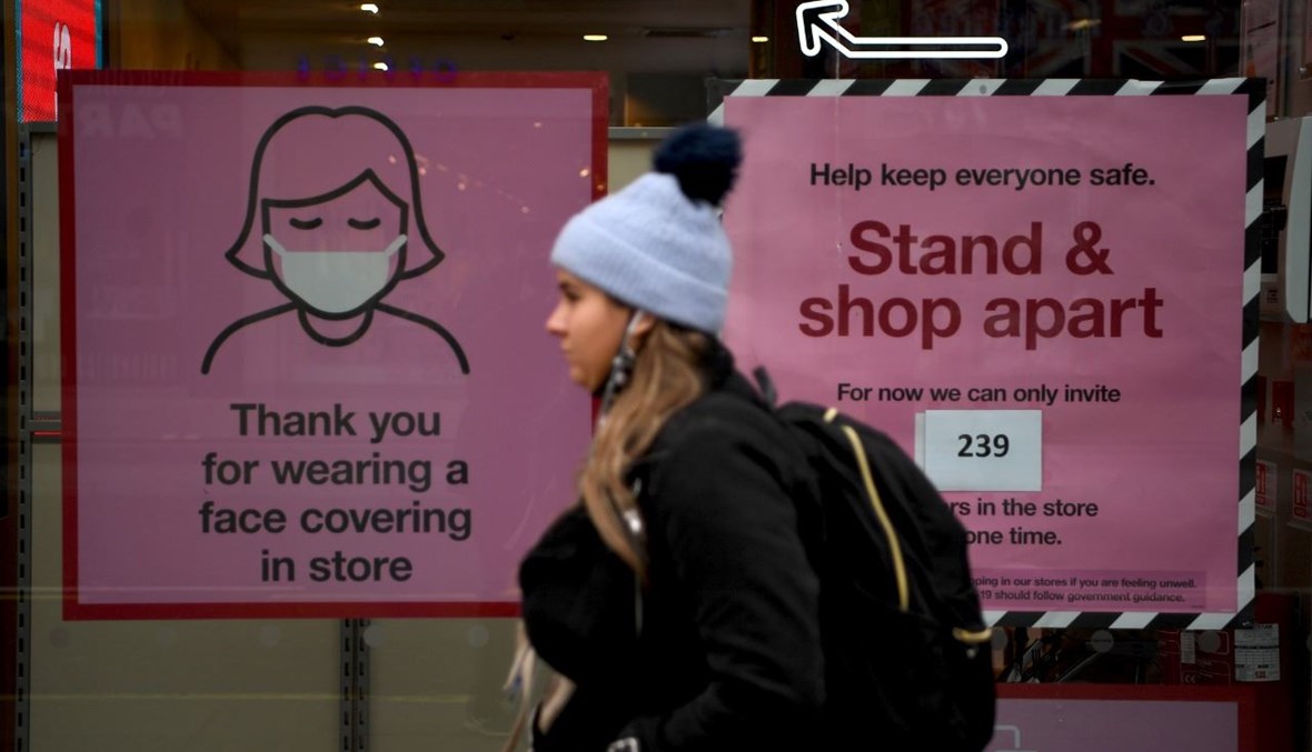امرأة تمر بالقرب من متجر مغلق في شارع أكسفورد بلندن، حيث  رفعت على واجهته مصلقات تنصح بوضع الكمامة (26 ت2 2020، أ ف ب). 