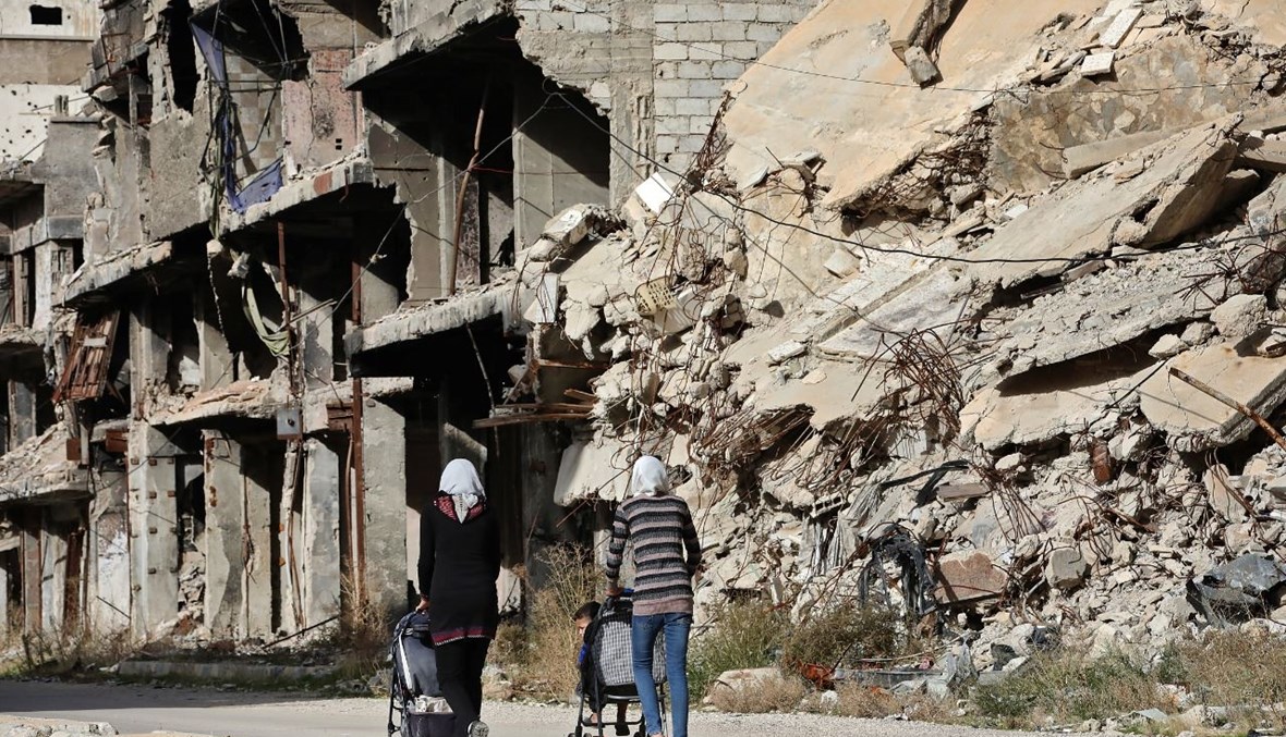 سكان في مخيم اليرموك الفلسطيني عند الأطراف الجنوبية لدمشق، يمرون بجوار بنايات مدمرة (25 ت2 2020، أ ف ب). 