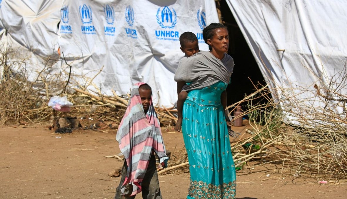 لاجئة أثيوبية تحمل طفلها على ظهرها خلال سيرها في مخيم أم الرقوبة في محافظة القضارف شرق السودان (28 ت2 2020، أ ف ب). 
