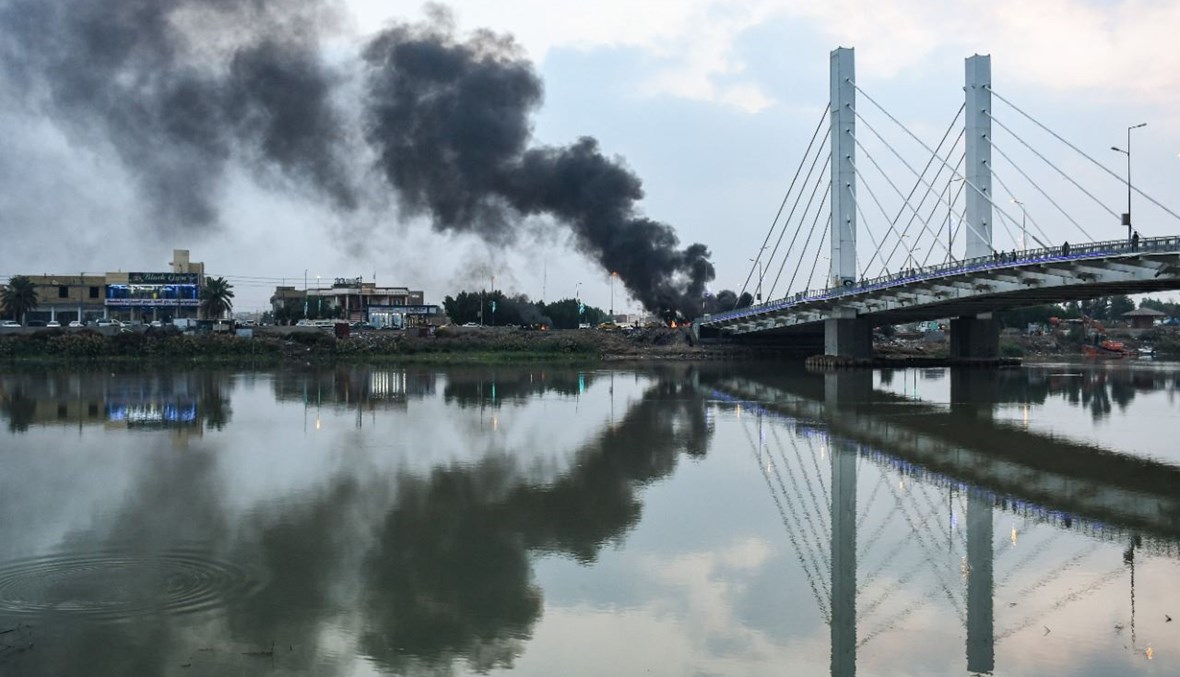 جسر الحضارات عند نهر الفرات، وقد تعالت خلفه أعمدة الدخان من موقع احتجاج مناهض للحكومة في ساحة الحبوبي في مدينة الناصرية جنوب العراق (29 ت2 2020، أ ف ب). 