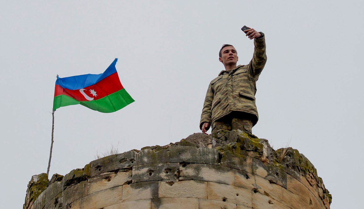 جندي أذربيجاني يلتقط صورة مع العلم الوطني فوق برج خارج مدينة فضولي (أ ف ب).