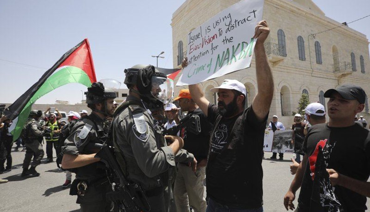 رجل حمل لافتة مناهضة لليوروفيجن في مواجة شرطيين إسرائيليين من حرس الحدود، بينما يحيي الفلسطينيون الذكرى الـ71 للنكبة (أ ب). 