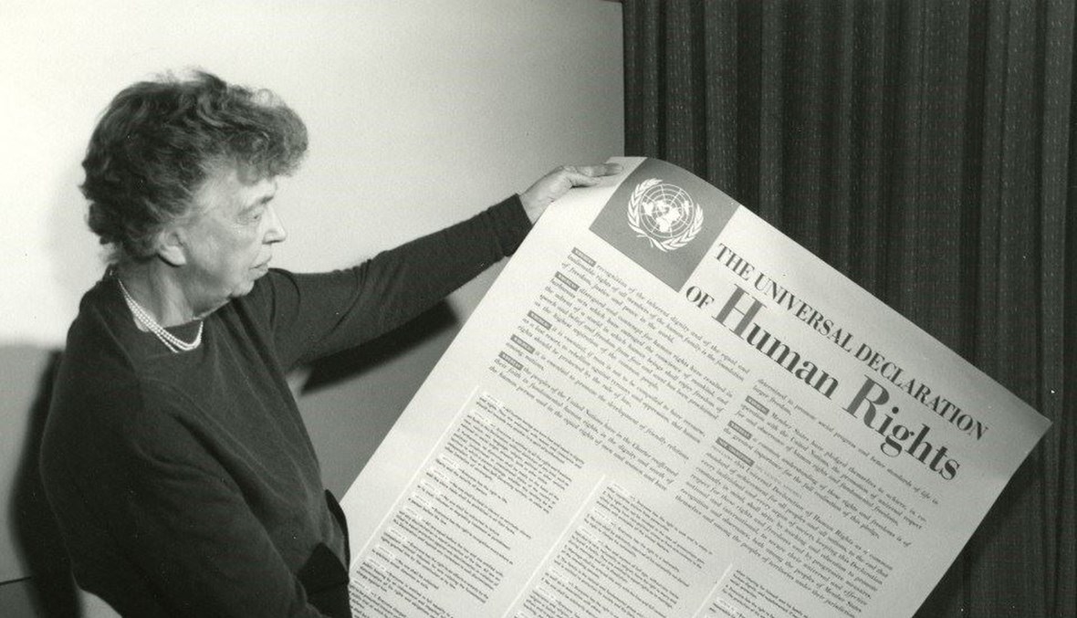 مفوّضة لجنة حقوق الإنسان إليانور روزفلت تحمل ملصق الإعلان العالمي لحقوق الإنسان باللغة الفرنسية، تشرين الثاني 1949، مقرّ الأمم المتحدة، نيويورك.