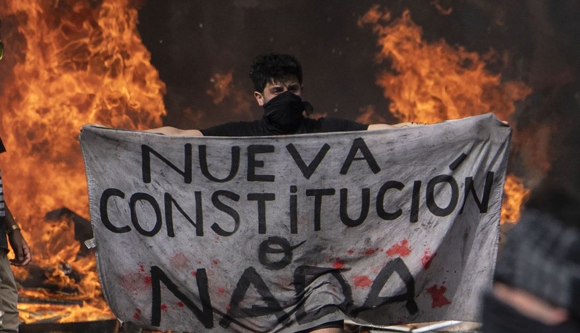 منظاهر في تشيلي يُطالب بالإصلاح حاملاً لافتة كُتب عليها: "إمّا دستور جديد أو لا شيء" (أ ف ب).