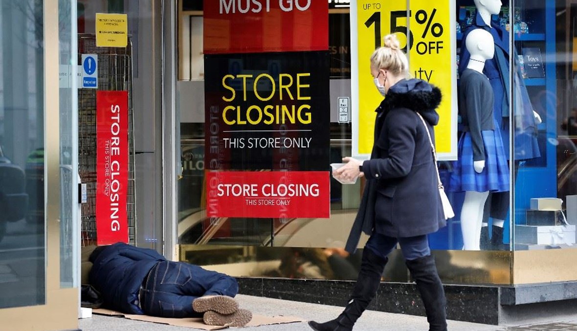 امرأة تضع كمامة واقية من كورونا تمر قبالة محل مغلق في وسط لندن وبدا أحد المشردين نائماً أمامه أمس.   (أ ف ب)