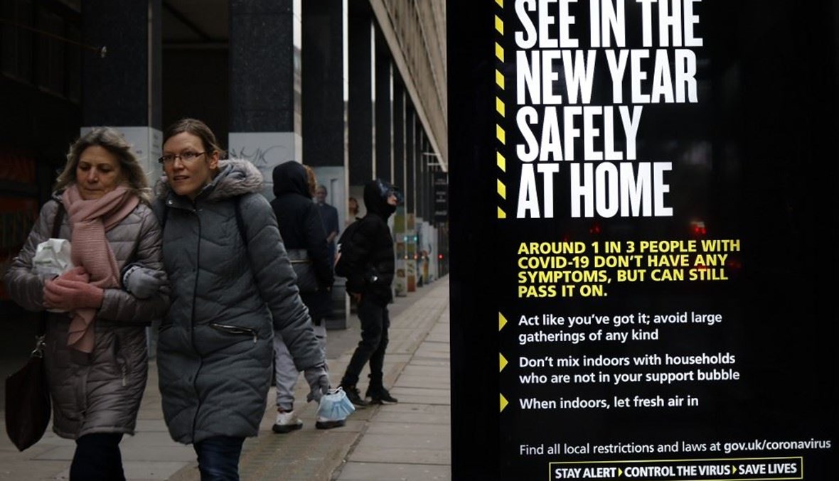 أشخاص يمرون قرب محطة للباصات في لندن وبدت لوحة اعلانية من الحكومة تحض على البقاء في المنزل في رأس السنة بلندن أمس.(أ ف ب)