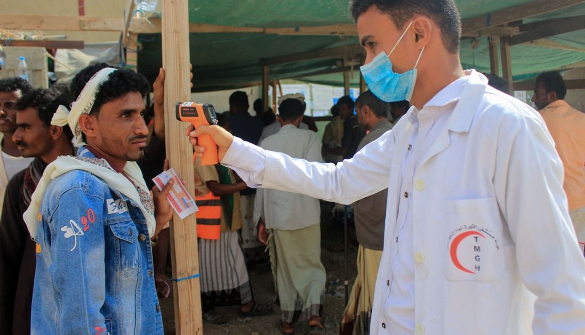عامل صحي يقيس حرارة نازح يمني في محافظة حجة الشمالية لدى وصوله لتسلم مساعدات إنسانية مقدمة من برنامج الغذاء العالمي (12 ك2 2021، أ ف ب).