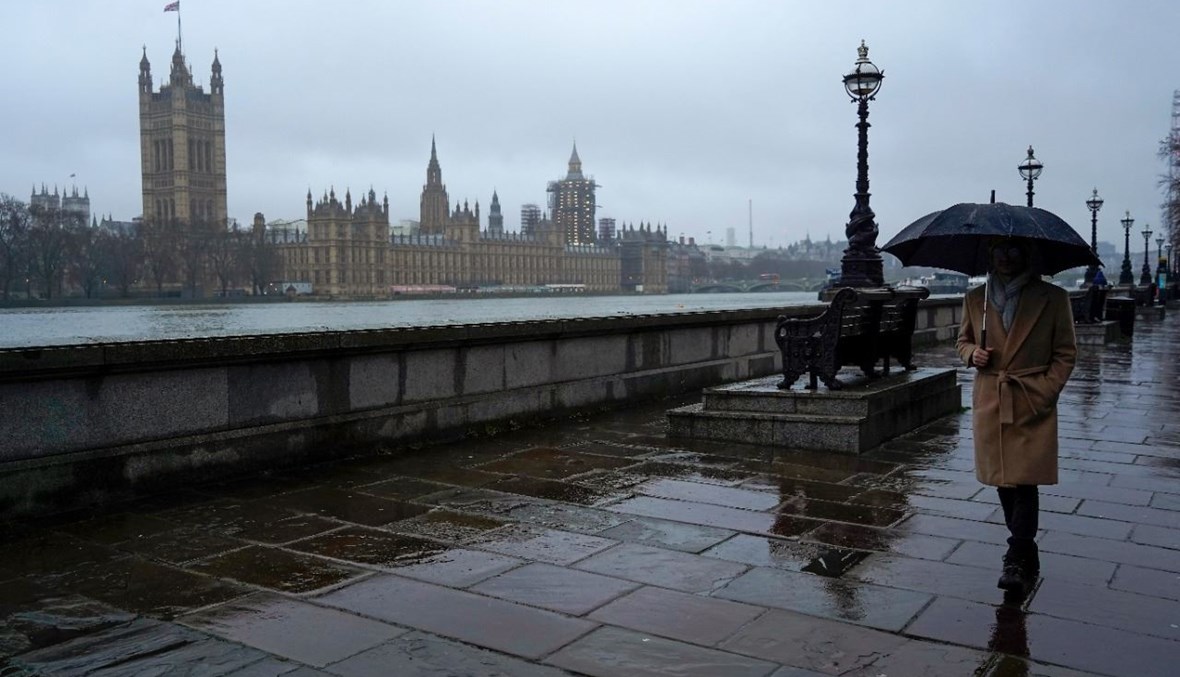 شخص يمشي تحت مظلة على الضفة الجنوبية لنهر التايمز بجوار مقر البرلمان في لندن (14 ك2 2021، أ ف ب). 