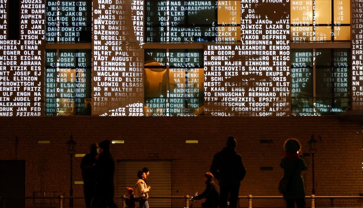 اشخاص يشاهدون عرضا ضوئيا يعرض أسماء ضحايا النظام النازي، في السفارة الفرنسية في برلين (21 ك2 2021، أ ف ب). 