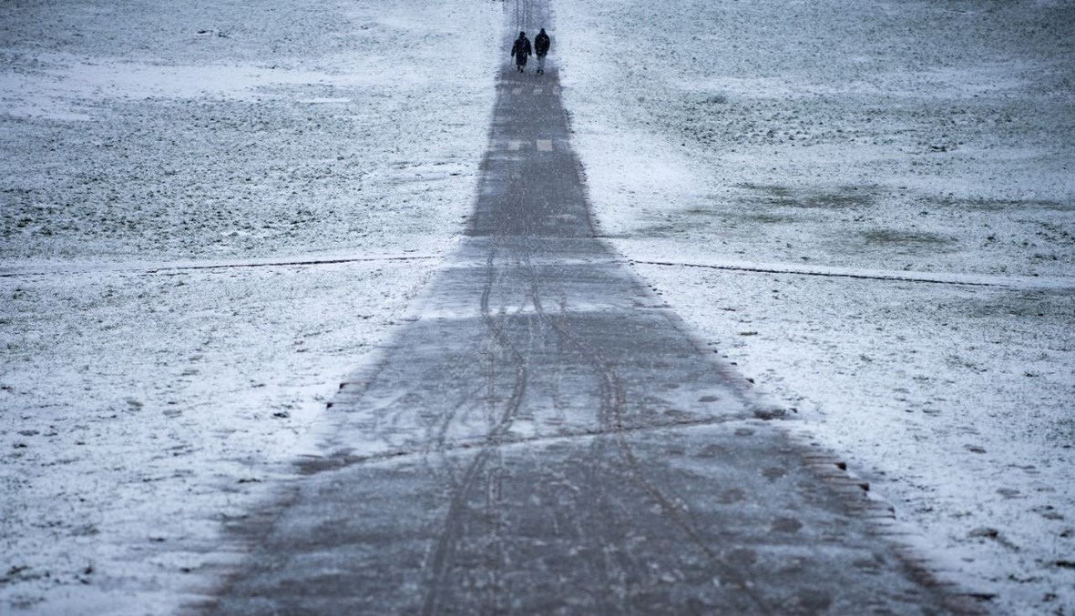 شخصان يمشيان في متنزه غويرليتسر في منطقة كروزبرغ في برلين أثناء تساقط الثلوج (19 ك2 2021، أ ف ب).
