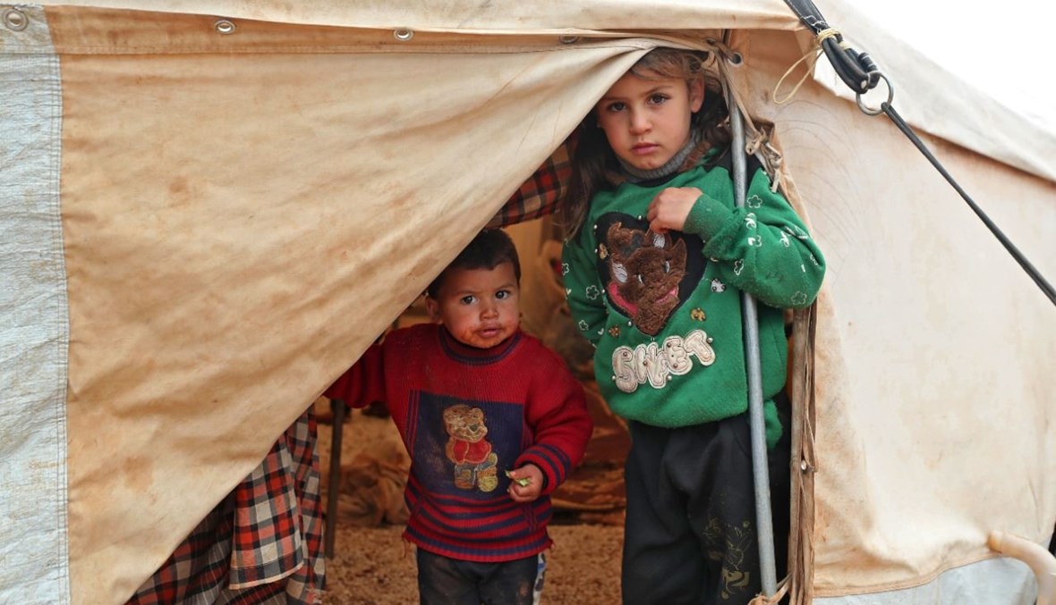 أطفال سوريون يقفون تحت خيمة بعد هطول أمطار غزيرة في مخيم الأمين في منطقة كفر عروق شمال غرب محافظة إدلب (19 ك2 2021، أ ف ب). 