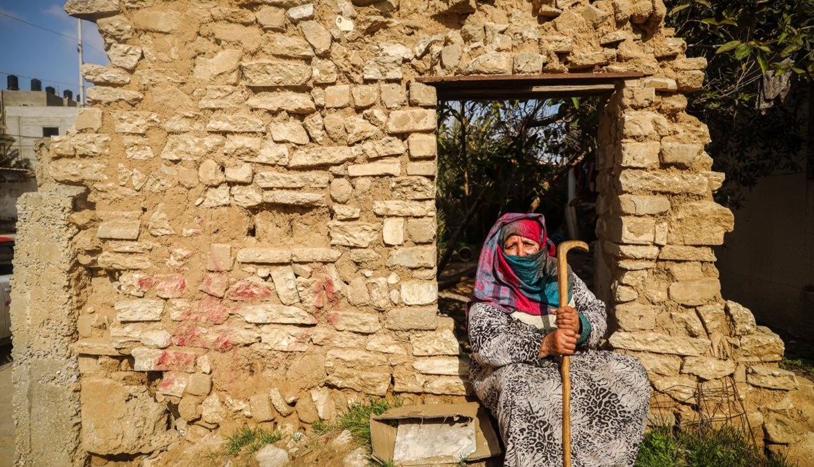 امرأة فلسطينية مسنة تجلس بجانب جدار مبنى مهدم بالقرب من منزلها في مدينة غزة (6 شباط 2021، أ ف ب).