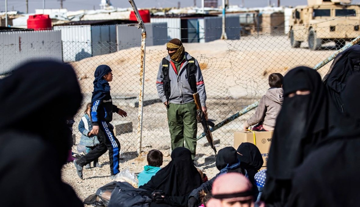 عنصر من الأمن الداخلي الكردي يقف للحراسة بينما تستعد نساء وأطفال لمغادرة من مخيم الهول في محافظة الحسكة في شمال شرق سوريا (28 ك2 2021، أ ف ب).