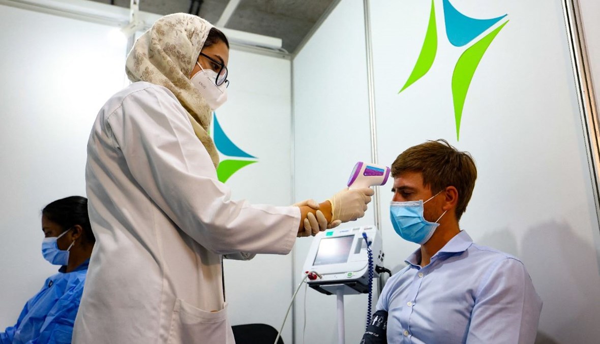 عاملة صحية تفحص حرارة رجل قبل تلقيه لقاح كورونا في مركز تطعيم في مركز دبي المالي العالمي في إمارة دبي (3 شباط 2021، أ ف ب).