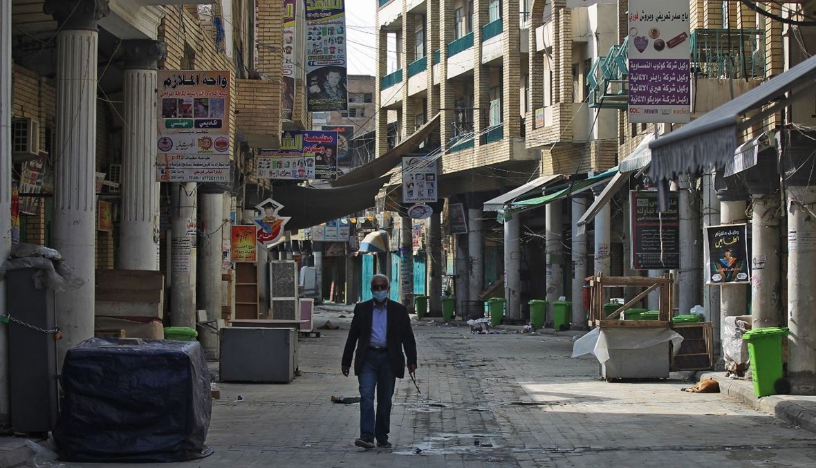 عراقي يمرّ بالقرب من محال تجارية مغلقة في بغداد (19 شباط 2021، أ ف ب).