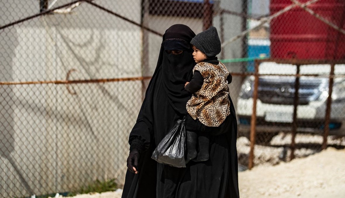 امرأة تحمل طفلًا وهي تمشي في مخيم الهول في محافظة الحسكة شمال شرق سوريا (3 آذار 2021، أ ف ب).