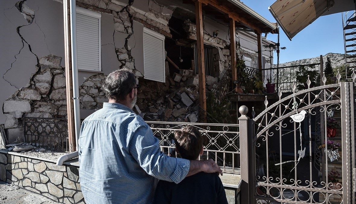 أب وابنه أمام منزل مدمّر في قرية دماسي، بالقرب من بلدة تيرنافوس، بعد الزلزال الذي ضرب منطقة ثيساليا اليونانية الوسطى (أ ف ب).